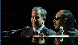 Mike and Stevie Wonder on stage sitting at a piano during the house Full of Toys Concert